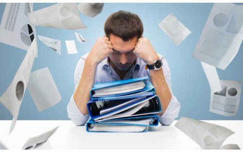 Stressed teacher over piles of paper work