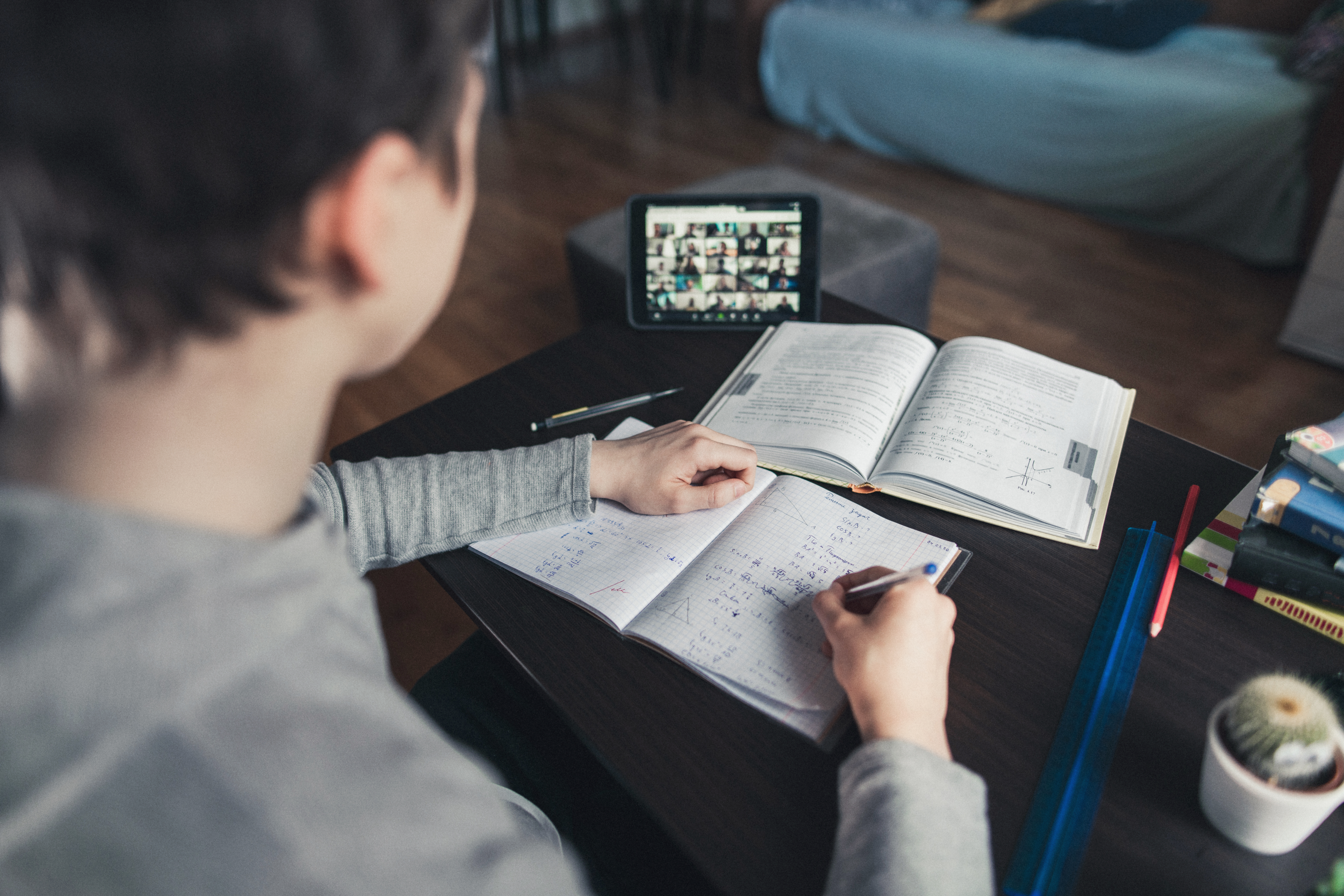 A boy makes notes whilst on a remote video call with class
