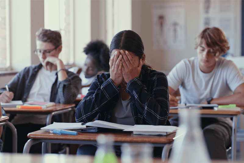 Stressed student in exam room holding his face in his hands