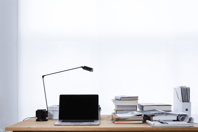 Desk with laptop, stack of books and notebooks