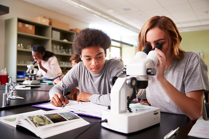 Students looking through a microscope and writing notes