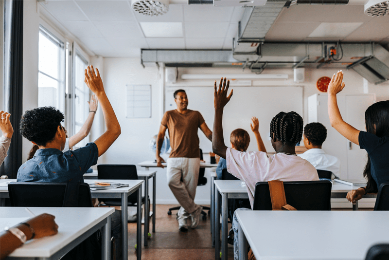 Classroom with students holding their hands up